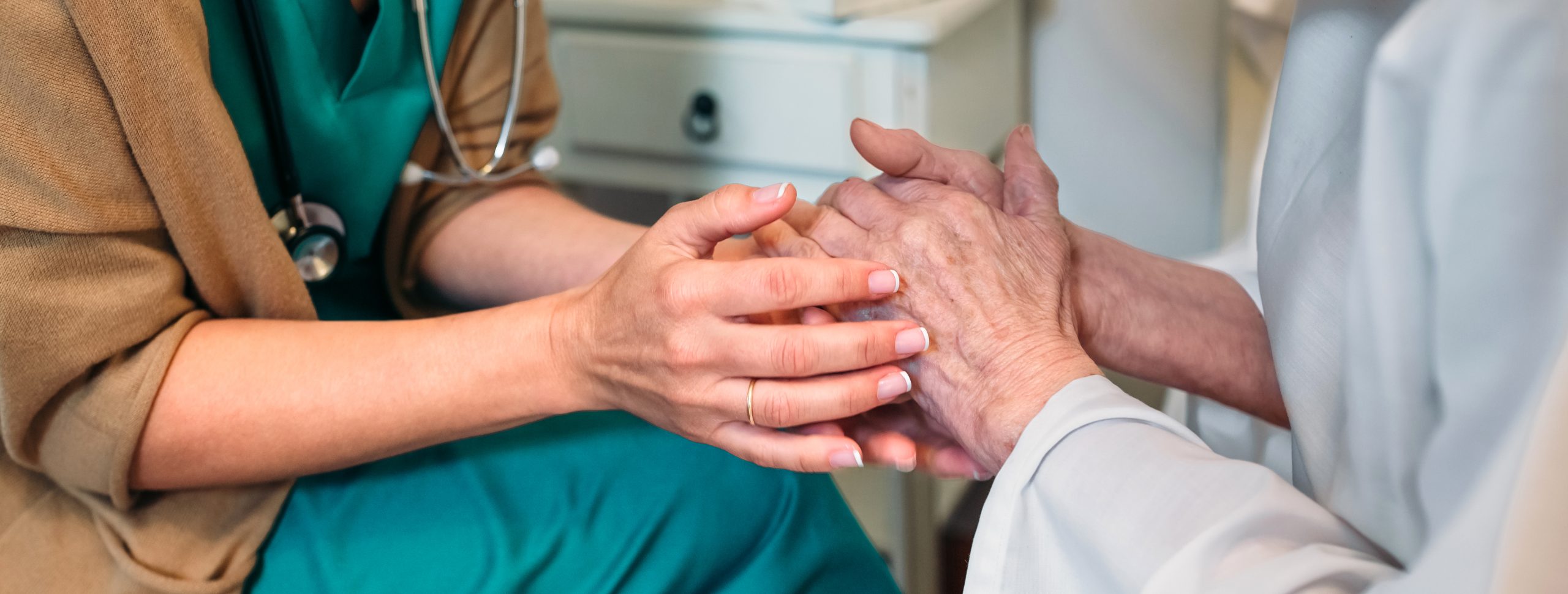 Female nurse giving encouragement to elderly patient by holding her hands